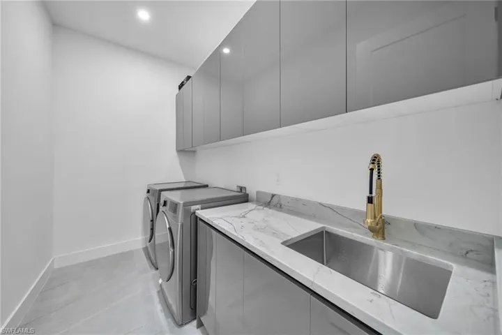 Clothes washing area featuring cabinets, washer and clothes dryer, and sink