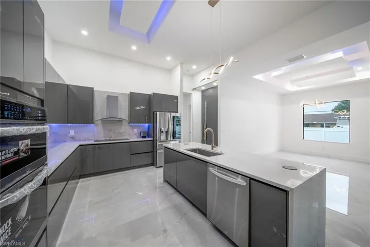 Kitchen with gray cabinets, sink, appliances with stainless steel finishes, a center island with sink, and wall chimney range hood