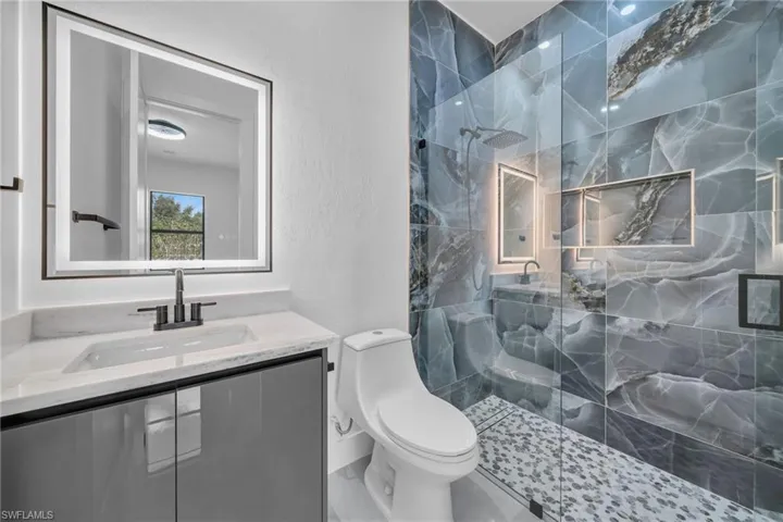 Bathroom featuring tiled shower, toilet, and vanity