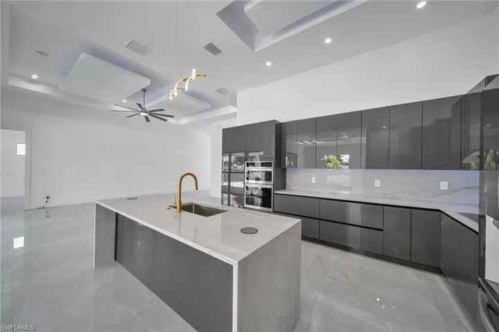 Kitchen with light stone counters, sink, gray cabinets, a spacious island, and ceiling fan