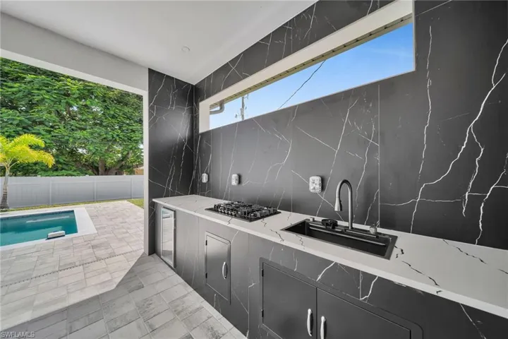 View of patio featuring a fenced in pool, sink, an outdoor kitchen, and wine cooler
