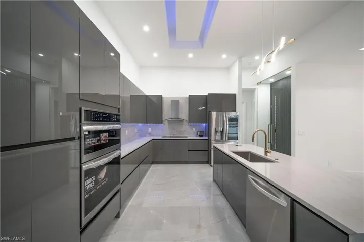 Kitchen with stainless steel appliances, sink, gray cabinets, light stone counters, and wall chimney range hood