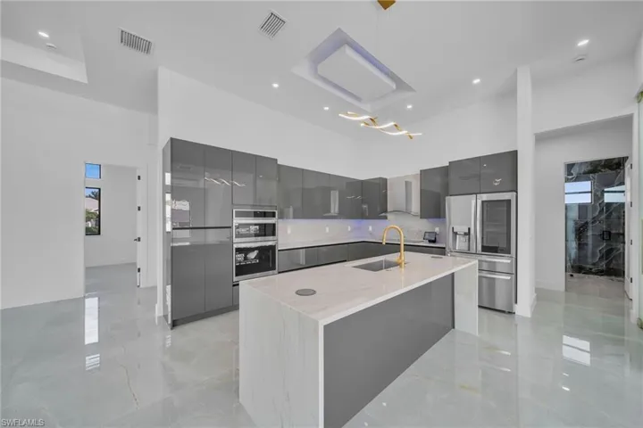 Kitchen featuring sink, gray cabinets, wall chimney range hood, pendant lighting, and a center island with sink