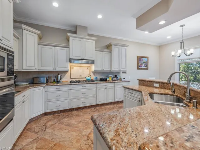 Kitchen featuring backsplash, an inviting chandelier, crown molding, sink, and white cabinetry