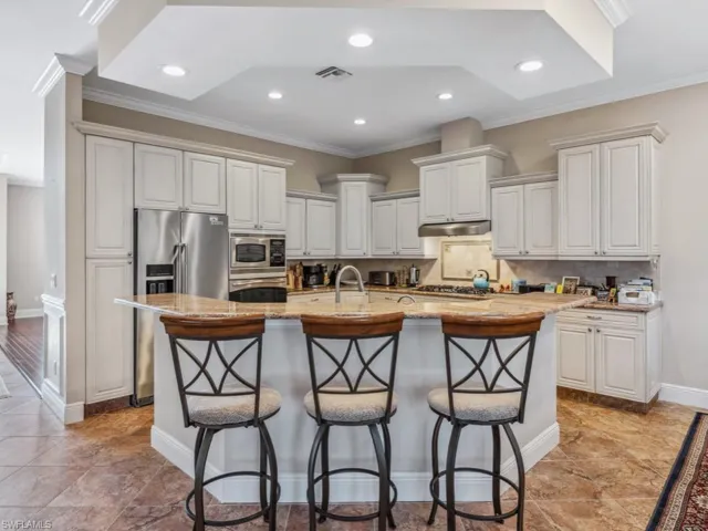 Kitchen featuring a center island with sink, a kitchen breakfast bar, decorative backsplash, white cabinetry, and stainless steel appliances