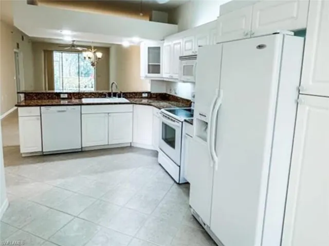 Kitchen with a sink, white cabinetry, dark countertops, and white appliances