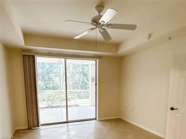 Empty room with baseboards, a ceiling fan, a tray ceiling, and light tile patterned floors