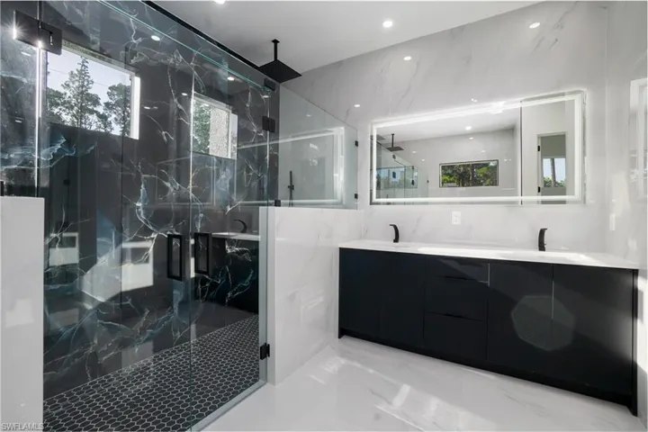 Full bath with a marble finish shower, double vanity, marble tiled floors, and recessed lighting