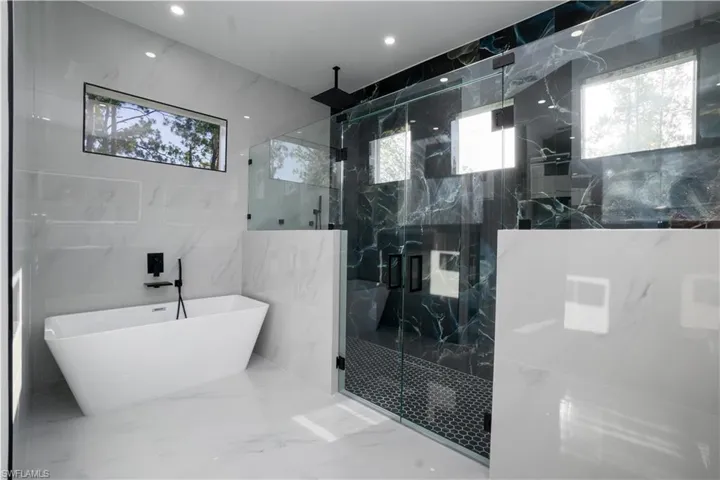 Bathroom with plenty of natural light, marble tiled floors, tile walls, a marble finish shower, and a freestanding bath