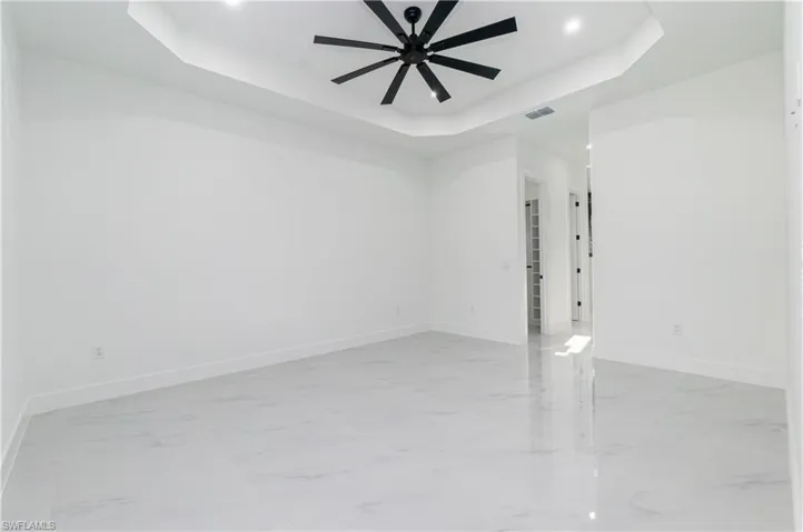 Empty room with a tray ceiling, light marble finish floors, ceiling fan, and recessed lighting