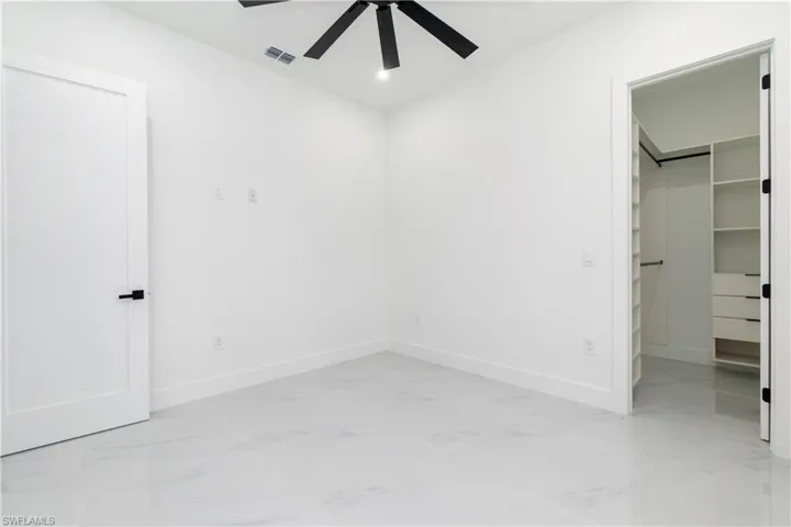 Unfurnished bedroom with a walk in closet, light marble finish floors, a ceiling fan, and recessed lighting