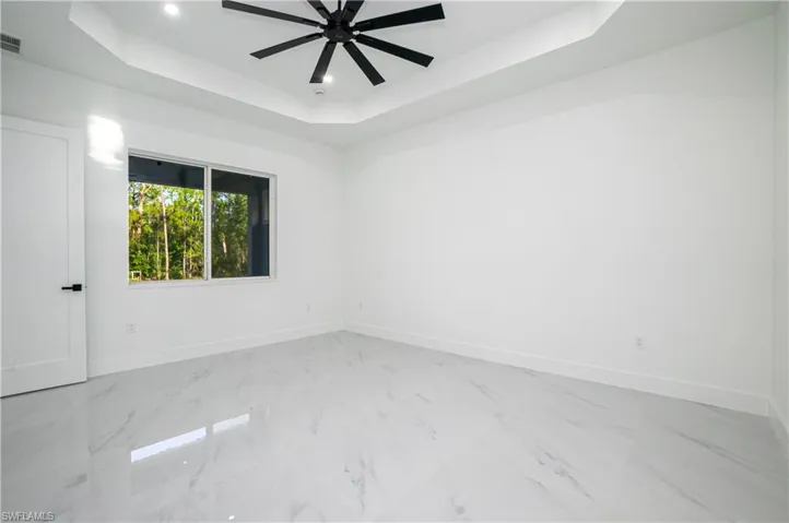 Spare room featuring a raised ceiling, ceiling fan, light marble finish floors, and recessed lighting