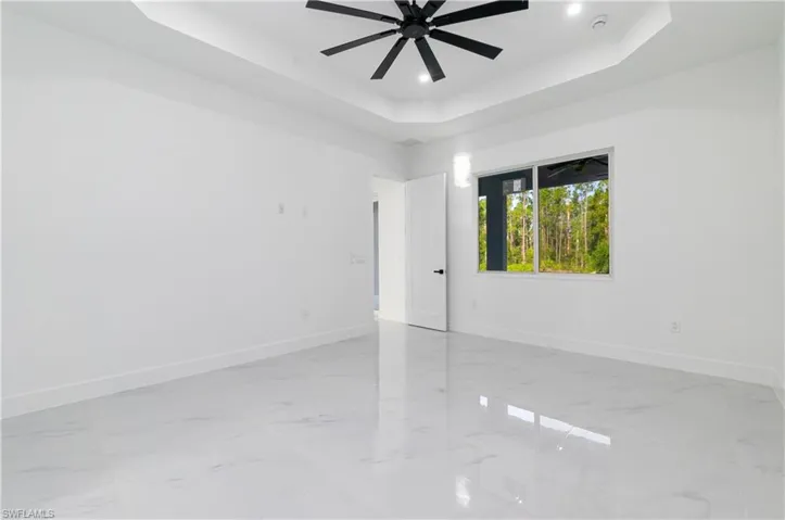 Spare room with a raised ceiling, light marble finish floors, ceiling fan, and recessed lighting