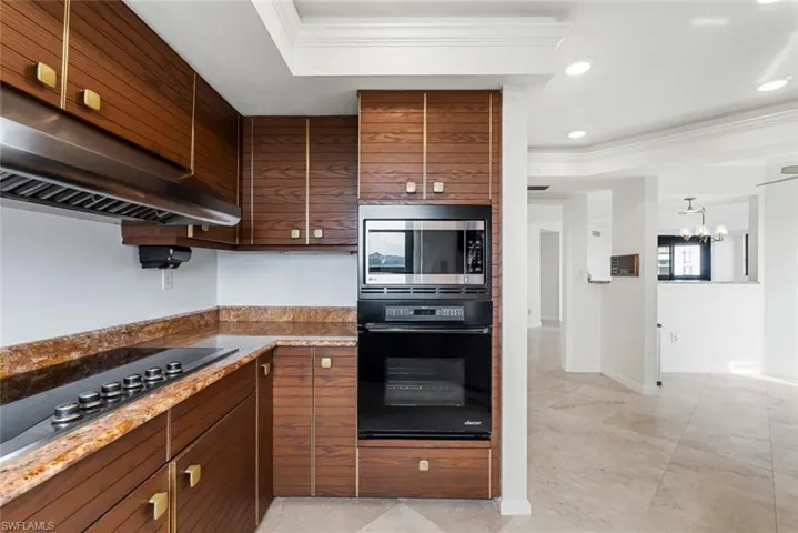 Kitchen featuring a raised ceiling, crown molding, a chandelier, extractor fan, and black appliances