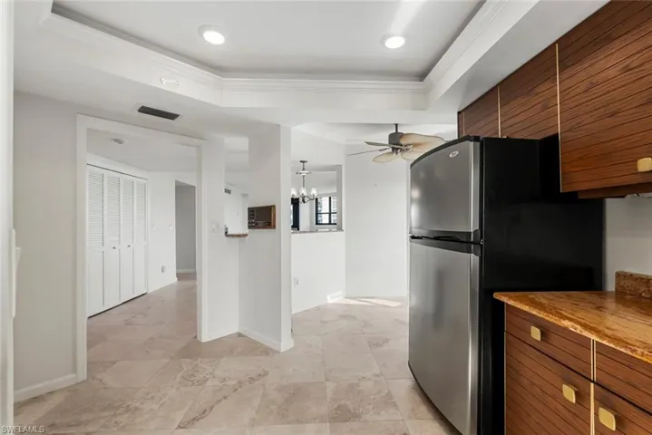 Kitchen with stainless steel fridge, ceiling fan with notable chandelier, a raised ceiling, and crown molding