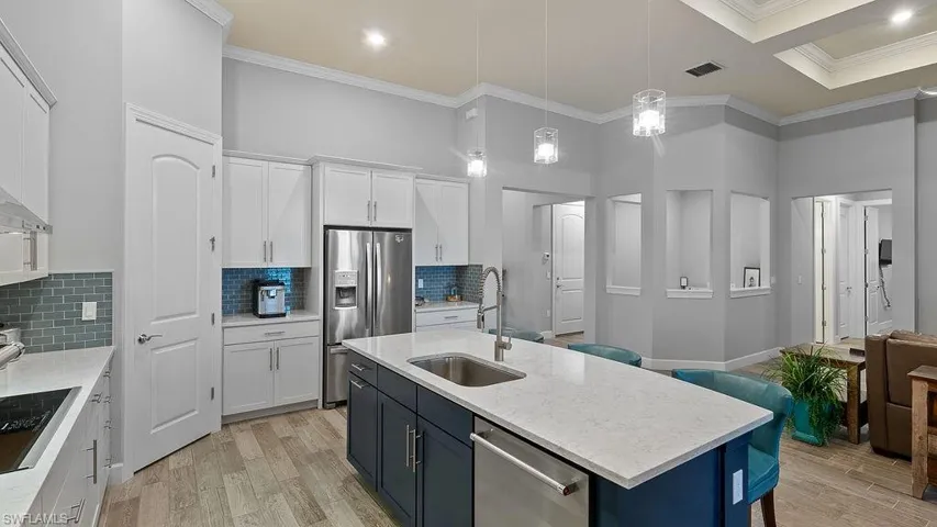 Kitchen with light hardwood / wood-style floors, appliances with stainless steel finishes, decorative backsplash, and a kitchen island with sink