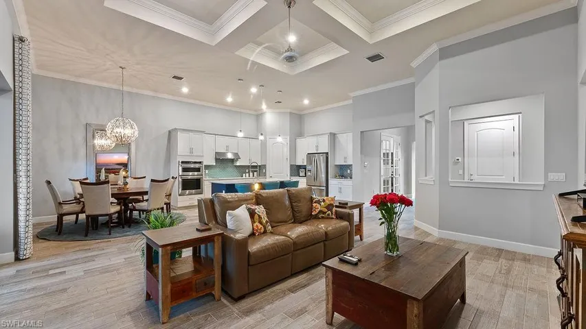 Living room with an inviting chandelier, sink, light hardwood / wood-style floors, ornamental molding, and coffered ceiling