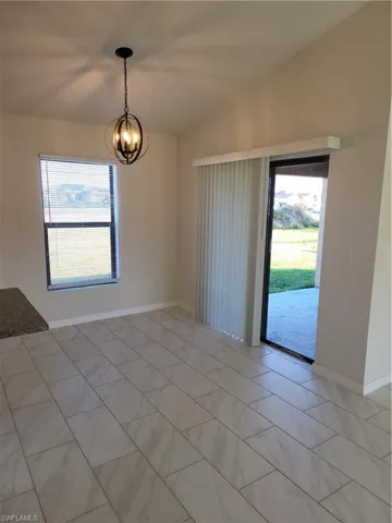 Unfurnished room featuring vaulted ceiling, plenty of natural light, and a chandelier
