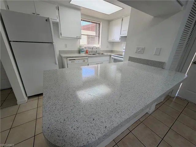 Kitchen with white appliances, a peninsula, white cabinets, light stone counters, and light tile patterned floors
