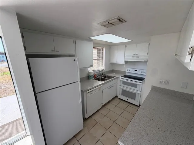 Kitchen with white appliances, light countertops, white cabinets, and light tile patterned flooring
