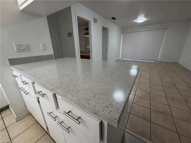 Kitchen with light tile patterned floors, a peninsula, white cabinetry, and light stone counters