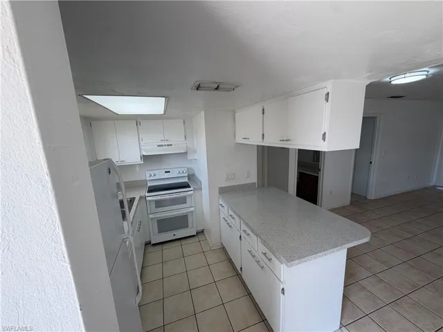Kitchen featuring white appliances, white cabinetry, a peninsula, and light tile patterned floors