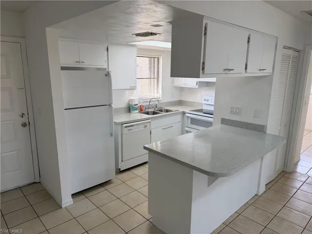 Kitchen featuring white appliances, white cabinets, light tile patterned floors, and a peninsula