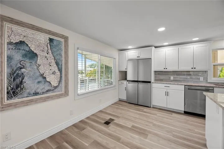 Kitchen featuring appliances with stainless steel finishes, white cabinets, light stone counters, light wood-type flooring, and backsplash