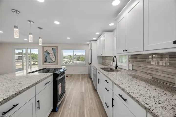 Kitchen with decorative light fixtures, black range with electric cooktop, white cabinets, light wood-type flooring, and recessed lighting