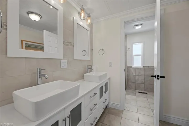 Full bath with tile walls, double vanity, ornamental molding, and light tile patterned floors