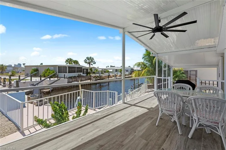 Wooden deck featuring outdoor dining area, a water view, ceiling fan, and a residential view