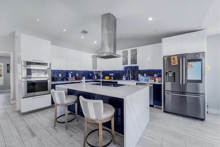 Kitchen featuring white cabinets, an island with sink, a breakfast bar, island range hood, and stainless steel appliances
