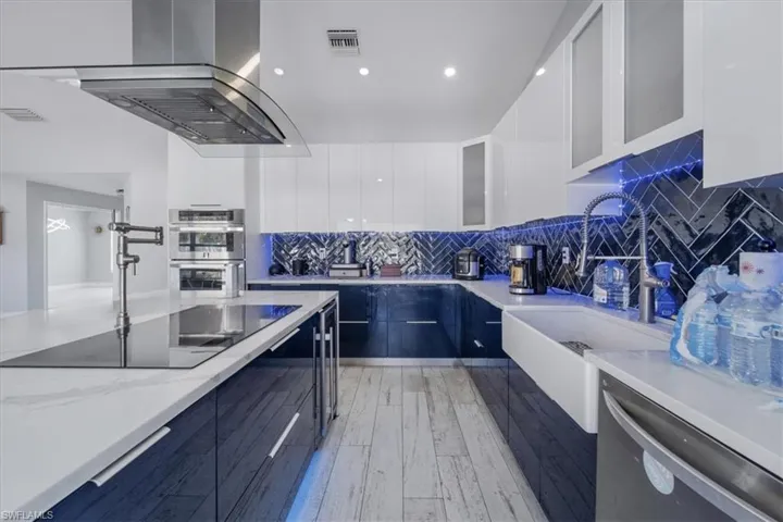 Kitchen with island range hood, a kitchen island with sink, white cabinetry, appliances with stainless steel finishes, and light hardwood / wood-style floors