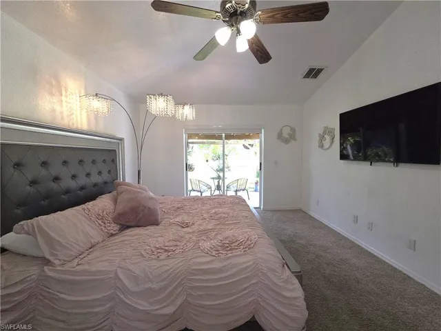 Carpeted bedroom featuring access to exterior, vaulted ceiling, and ceiling fan