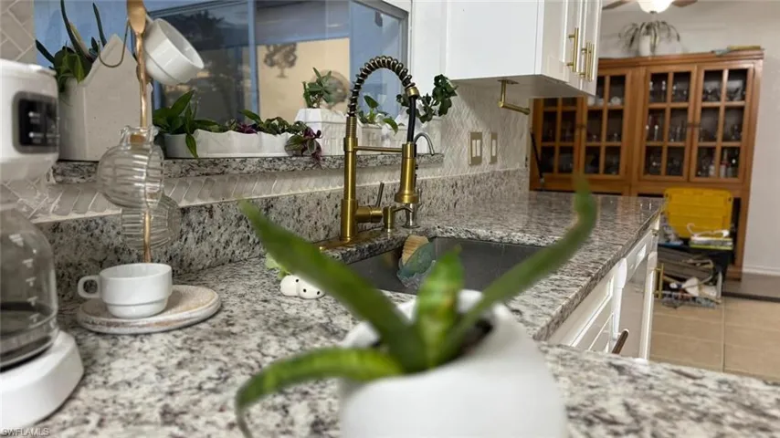 Kitchen view of white cabinetry, dishwasher, and light stone counters