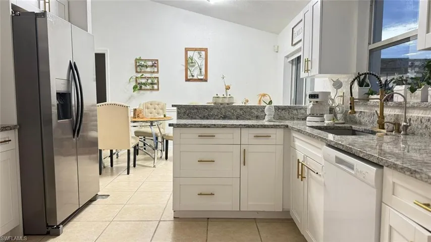 Kitchen featuring stainless steel refrigerator with ice dispenser, vaulted ceiling, dishwasher, a peninsula, and light tile patterned floors