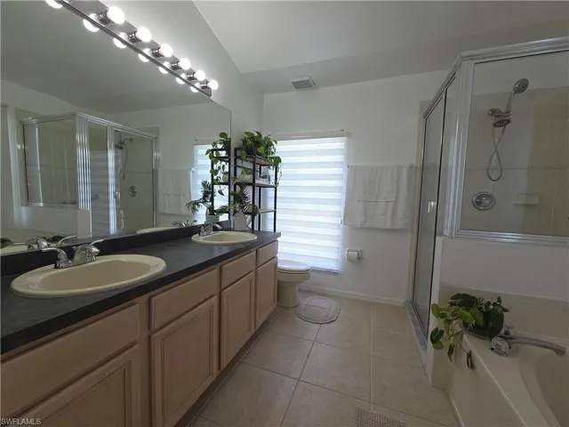 Full bath featuring tile patterned flooring, a stall shower, double vanity, and a garden tub