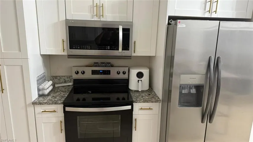 Kitchen with appliances with stainless steel finishes, white cabinetry, and dark stone countertops