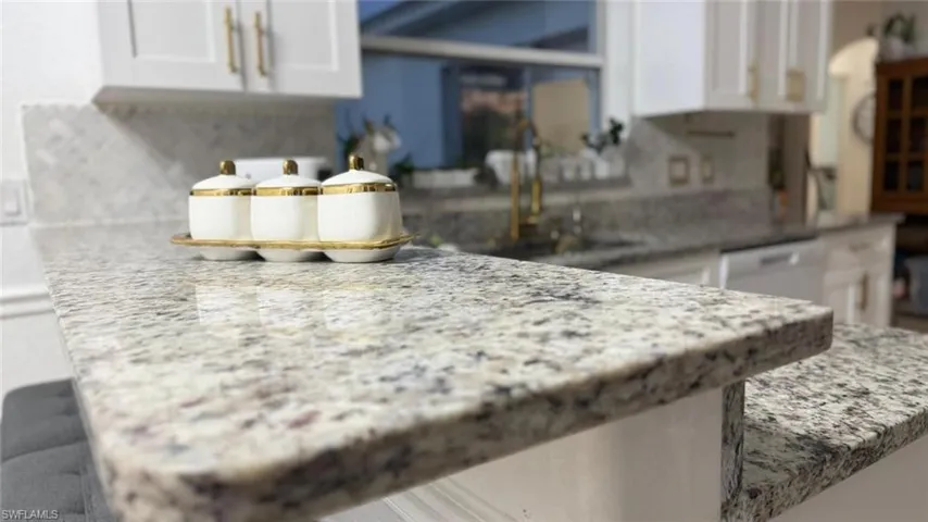 Kitchen view of white cabinetry, backsplash, white dishwasher, and light stone countertops