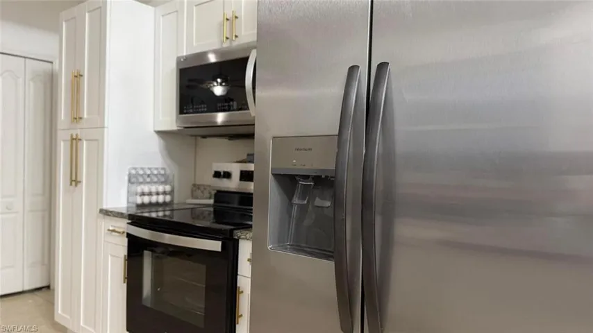 Kitchen with stainless steel appliances, dark stone countertops, white cabinetry, and light tile patterned floors