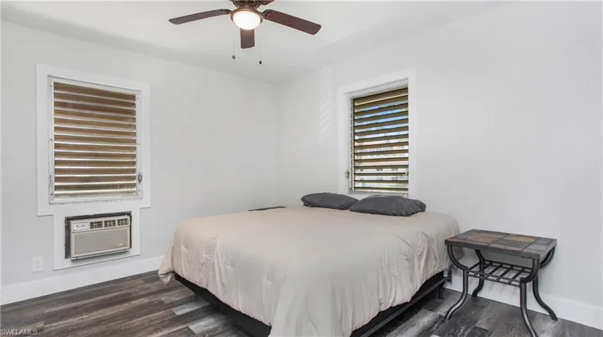 Bedroom 1 with 5" baseboards, wood-style flooring, a wall mounted air conditioner, and ceiling fan