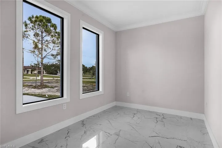 Empty room with crown molding, marble finish floor, a healthy amount of sunlight, and baseboards