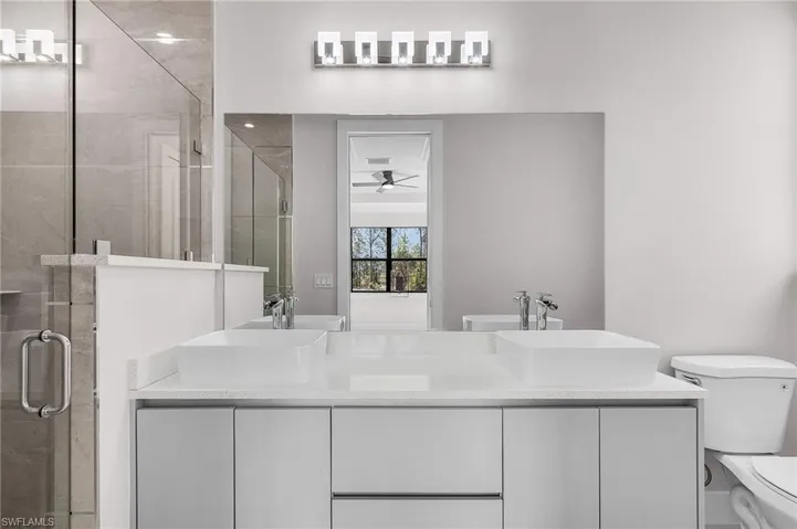 Full bathroom featuring a stall shower, a ceiling fan, double vanity, and a sink