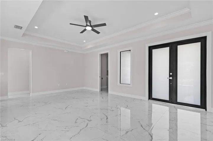 Empty room with marble finish floor, ornamental molding, baseboards, visible vents, and a ceiling fan