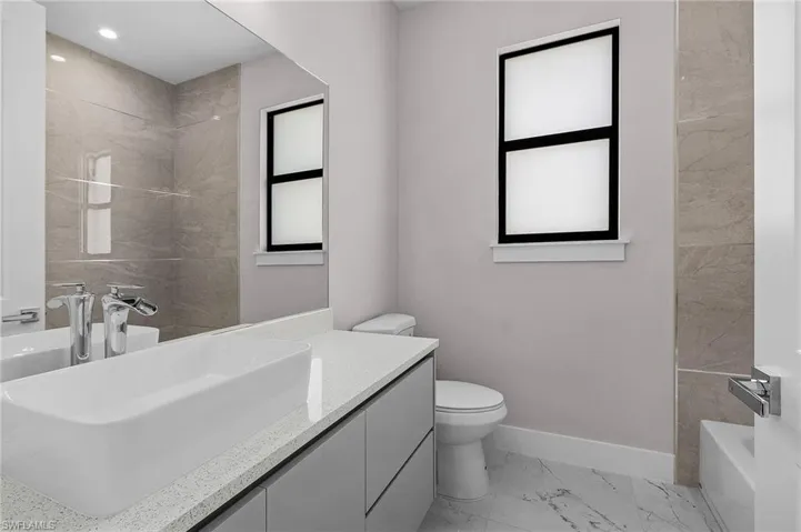 Full bath featuring marble finish floor, a tub to relax in, toilet, vanity, and baseboards