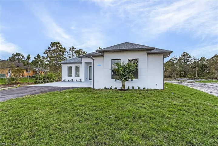 View of front of house featuring stucco siding, a front yard, and a shingled roof