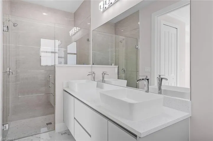 Bathroom with double vanity, marble finish floor, a stall shower, and a sink