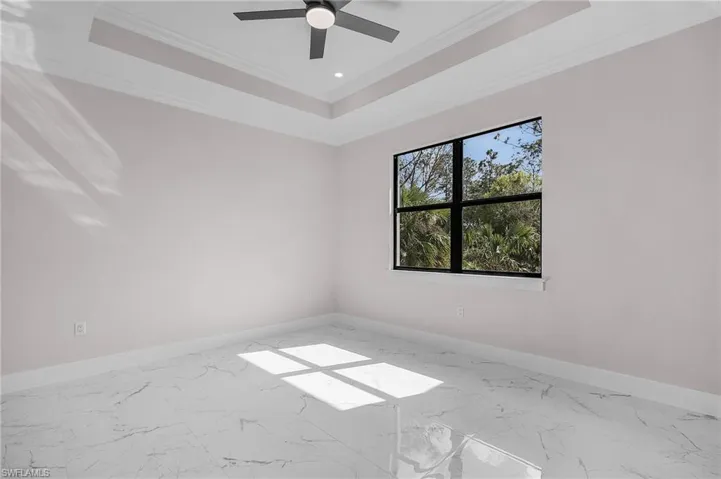 Unfurnished room featuring ceiling fan, a tray ceiling, baseboards, ornamental molding, and marble finish floor