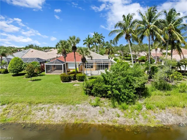 Back of house with a water view, a lawn, glass enclosure, and a tile roof