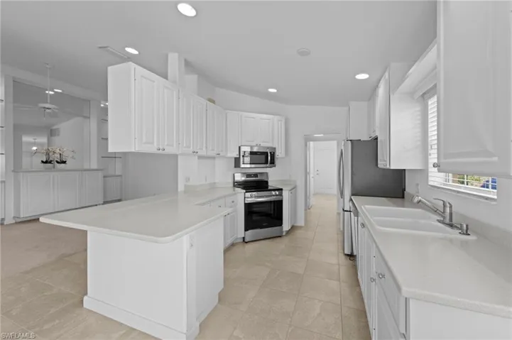 Kitchen with appliances with stainless steel finishes, a peninsula, white cabinets, recessed lighting, and light countertops